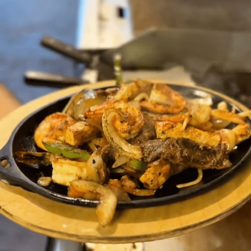 Sizzling fajitas with shrimp, steak, onions, and bell peppers on a hot cast iron plate.