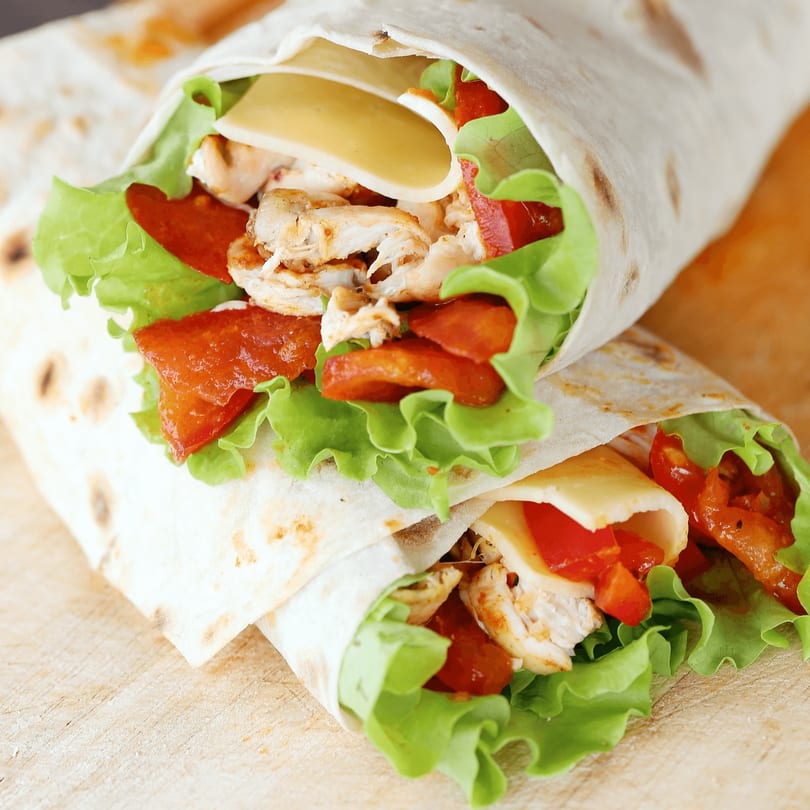 Two chicken wraps with lettuce, tomatoes, and cheese, on a wooden surface.